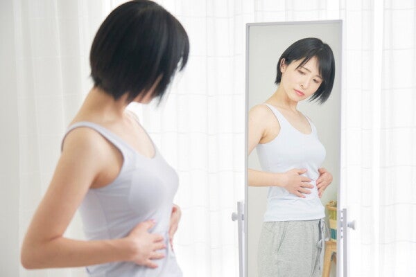 A young Asian woman looking at her belly in the mirror at home.
