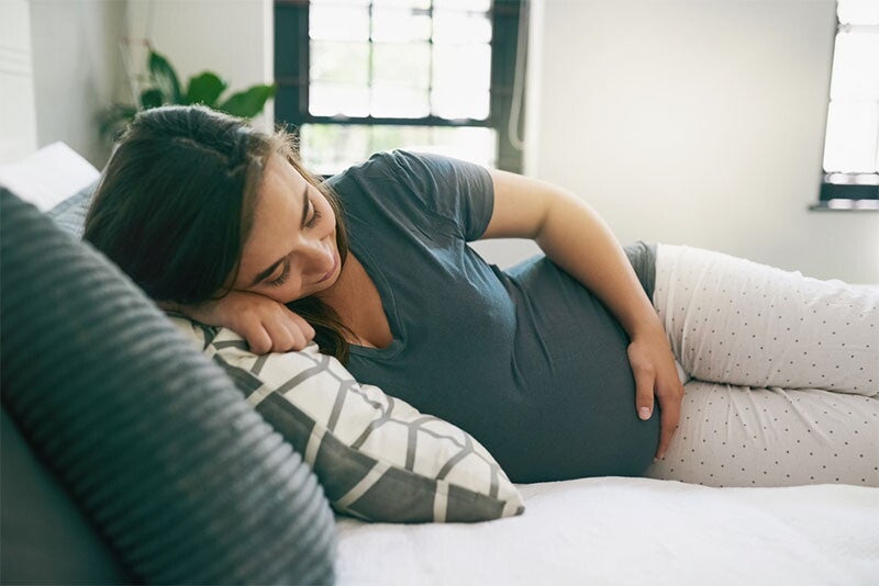 Asian pregnant female lies on her side cradling her baby bump