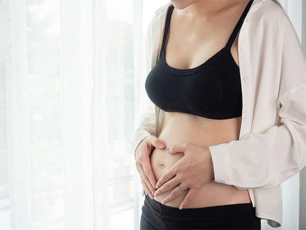 Cropped photo of a 6 weeks pregnant Asian woman’s torso with her hands on her belly