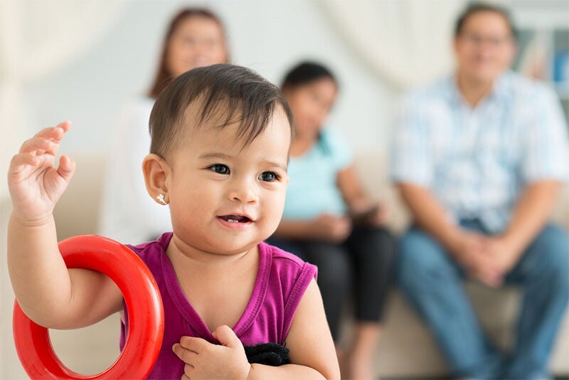 Female toddler with traditional Filipino name plays with stacking rings as her family watches in the background