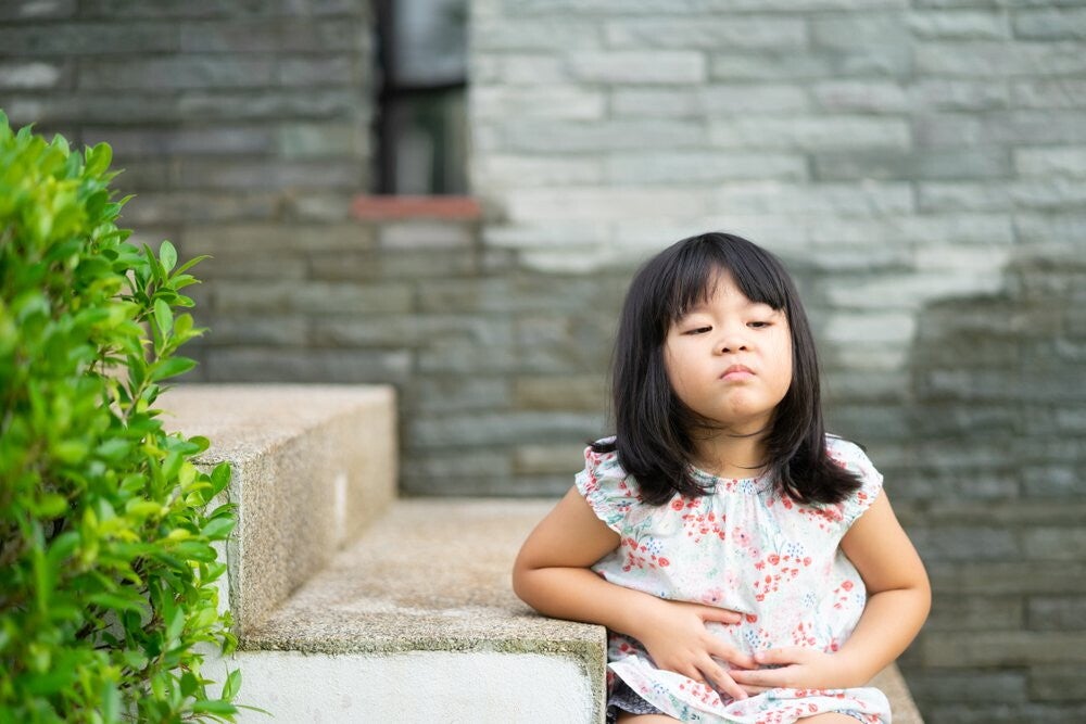 Asian preschool-age girl winces as if in pain while touching her stomach.