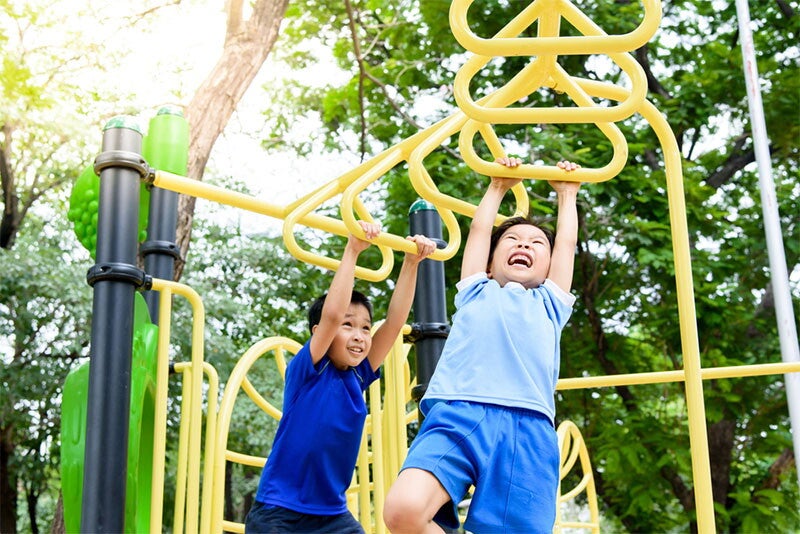 Two Asian kids hang onto monkey bars as part of their exercise