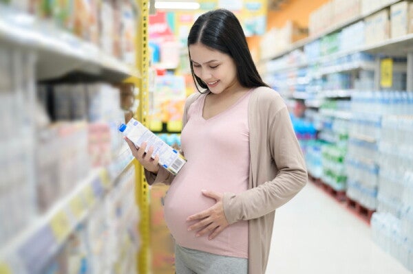 A young pregnant Asian woman looking at food labels in a grocery store.