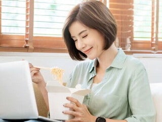 Young Filipina experiences a food craving and enjoys takeout while sitting on the sofa with her laptop on her lap. Young Filipina experiences a food craving and enjoys takeout while sitting on the sofa with her laptop on her lap.