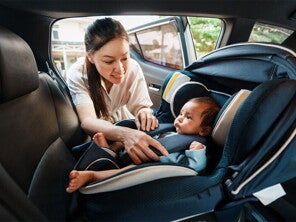 An Asian woman fastening her infant into a rear-facing car seat. An Asian woman fastening her infant into a rear-facing car seat.