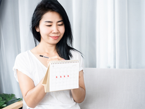 Asian woman checking the calendar for ovulation or menstruation to understand PMS symptoms vs pregnancy symptoms Asian woman checking the calendar for ovulation or menstruation to understand PMS symptoms vs pregnancy symptoms