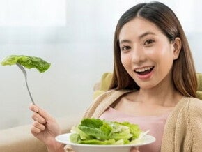Asian pregnant woman eating greens on sofa. Asian pregnant woman eating greens on sofa.