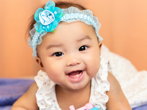 A smiling Asian little girl on her tummy, showing off baby’s first tooth A smiling Asian little girl on her tummy, showing off baby’s first tooth