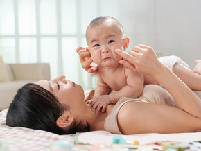 A young Asian mom lying in bed keeping her tearful baby close to her, knowing why babies cry A young Asian mom lying in bed keeping her tearful baby close to her, knowing why babies cry