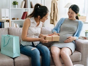 A young Asian pregnant woman receiving a gift from her friend during her baby shower at home. A young Asian pregnant woman receiving a gift from her friend during her baby shower at home.