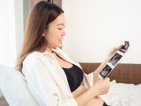 A young Asian woman in bed looking at her ultrasound at 13 weeks pregnant A young Asian woman in bed looking at her ultrasound at 13 weeks pregnant