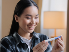 A young Asian woman smiling as she looks at a pregnancy test and curious about the stages of pregnancy. A young Asian woman smiling as she looks at a pregnancy test and curious about the stages of pregnancy.