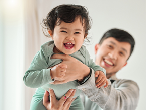 Asian dad lifts his laughing baby with both hands high in the air  Asian dad lifts his laughing baby with both hands high in the air