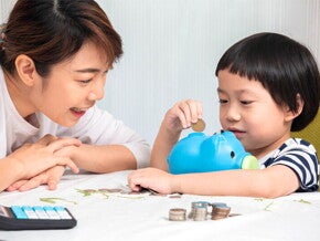 Asian mom and son putting coins in piggy bank