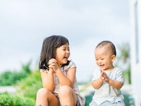 Asian preschool-age girl and her baby brother laugh as they play a game outdoors Asian preschool-age girl and her baby brother laugh as they play a game outdoors