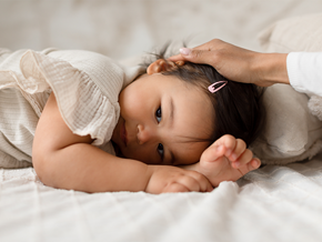 Asian toddler with respiratory tract infection lies face down as her parent strokes her head Asian toddler with respiratory tract infection lies face down as her parent strokes her head