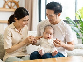 Filipino mom smiles at her newborn who's being held by her husband on his lap. Filipino mom smiles at her newborn who's being held by her husband on his lap.