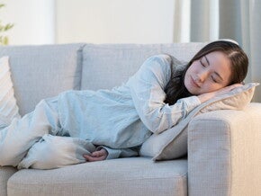 Young Asian woman falls asleep on the sofa, exhibiting an early sign of pregnancy.