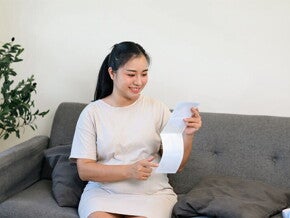 Young Asian pregnant woman on the sofa, holding her tummy and looking at her ultrasound scan at 28 weeks pregnant Young Asian pregnant woman on the sofa, holding her tummy and looking at her ultrasound scan at 28 weeks pregnant