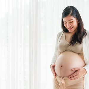 A 31 weeks pregnant Asian woman standing by the window, holding her large belly bump A 31 weeks pregnant Asian woman standing by the window, holding her large belly bump