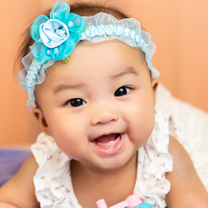 A smiling Asian little girl on her tummy, showing off baby’s first tooth A smiling Asian little girl on her tummy, showing off baby’s first tooth