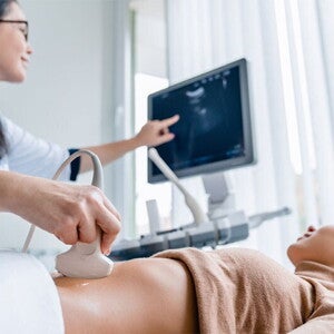 A smiling Asian pregnant woman undergoes an ultrasound scan with her ob-gyn for pregnancy complications