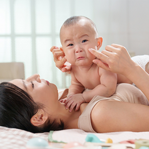 A young Asian mom lying in bed keeping her tearful baby close to her, knowing why babies cry A young Asian mom lying in bed keeping her tearful baby close to her, knowing why babies cry
