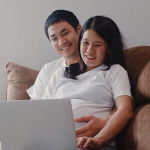 A young Asian pregnant couple with a laptop at home, applying online for the expanded maternity leave
