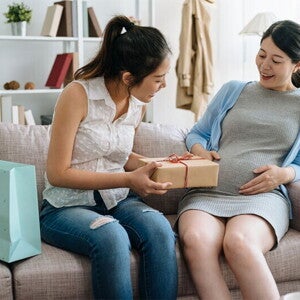A young Asian pregnant woman receiving a gift from her friend during her baby shower at home.