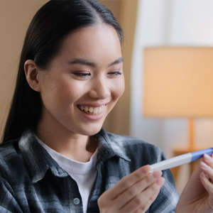 A young Asian woman smiling as she looks at a pregnancy test and curious about the stages of pregnancy. A young Asian woman smiling as she looks at a pregnancy test and curious about the stages of pregnancy.