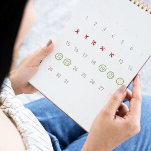 An Asian woman holding a calendar marked to show her menstrual cycle and fertile window