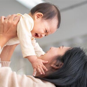 Asian baby girl grabs her mom's face as her mom lifts her
