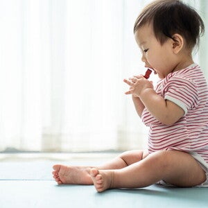 Asian baby sitting on a mat about to put a choking hazard in his mouth