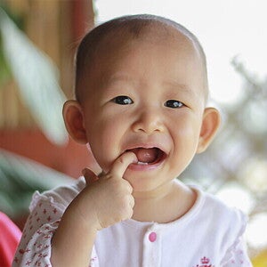 Asian baby with one of their fingers in their mouth.