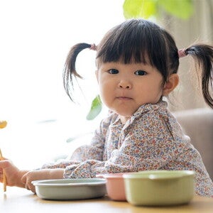 Asian female toddler prepares to eat as she holds her fork with food