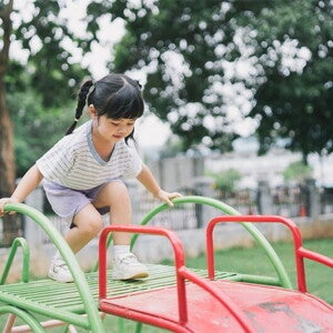 Asian girl, who doesn't show any signs of low calcium, climbs up the slide at a playground.