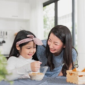 Asian mother watching her child eating cereal from a bowl