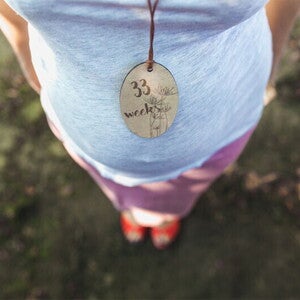 Cropped photo of pregnant Asian woman's belly wearing a necklace with a tag that says 33 weeks pregnant. Cropped photo of pregnant Asian woman's belly wearing a necklace with a tag that says 33 weeks pregnant.