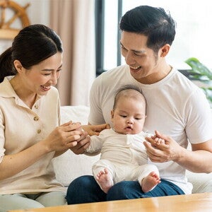 Filipino mom smiles at her newborn who's being held by her husband on his lap.