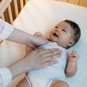 Asian baby being put to sleep on their back in safe crib.