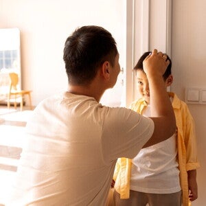 Asian dad marks his son's height on the wall to record growth milestone.