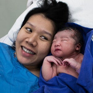 Smiling Asian mom glances at her newborn after skin-to-skin contact in the delivery room