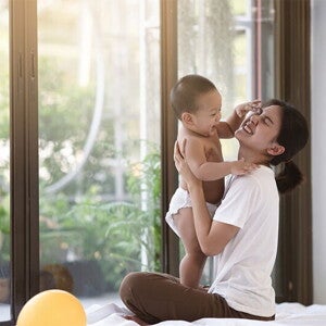Smiling Asian mom holding her clapping baby while seated on cushions on the floor
