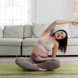 Smiling Asian pregnant woman who is 9 weeks pregnant performs yoga at home