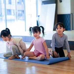 Three Adorable Asian preschoolers with healthy tummies sit on a yoga mat in fitness studio