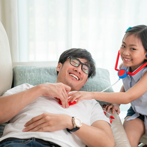 Young Asian girl listens to her father's heartbeat with a toy stethoscope, pretending to do dad’s medical checkups