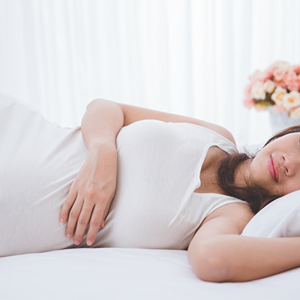 Young pregnant Asian woman lies on her left side in bed, one of the ideal pregnancy sleeping positions Young pregnant Asian woman lies on her left side in bed, one of the ideal pregnancy sleeping positions