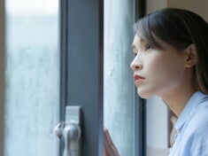 A young Asian woman, looking out at the rain, wondering what typhoon safety precautions to take for her family.