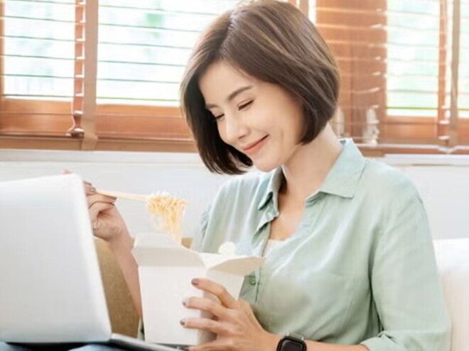Young Filipina experiences a food craving and enjoys takeout while sitting on the sofa with her laptop on her lap. Young Filipina experiences a food craving and enjoys takeout while sitting on the sofa with her laptop on her lap.